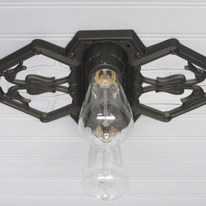 May include: A black metal ceiling light fixture with a decorative design. The fixture has a single bulb and is mounted to a white ceiling.