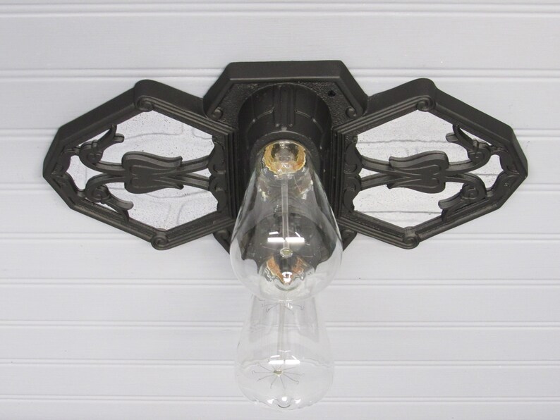 May include: A black metal ceiling light fixture with a decorative design. The fixture has a single bulb and is mounted to a white ceiling.
