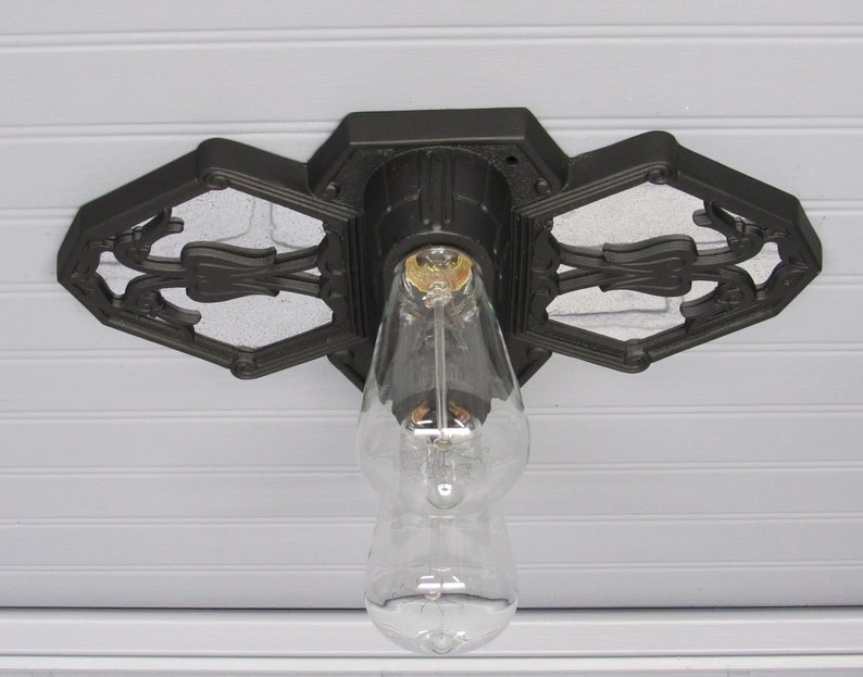 May include: Black ceiling light fixture with a decorative, ornate design. The fixture has a single light bulb and is mounted to a white ceiling.