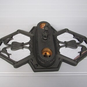 May include: A black metal ceiling light fixture with three decorative glass panels and two light sockets. The fixture has a decorative finial on top.