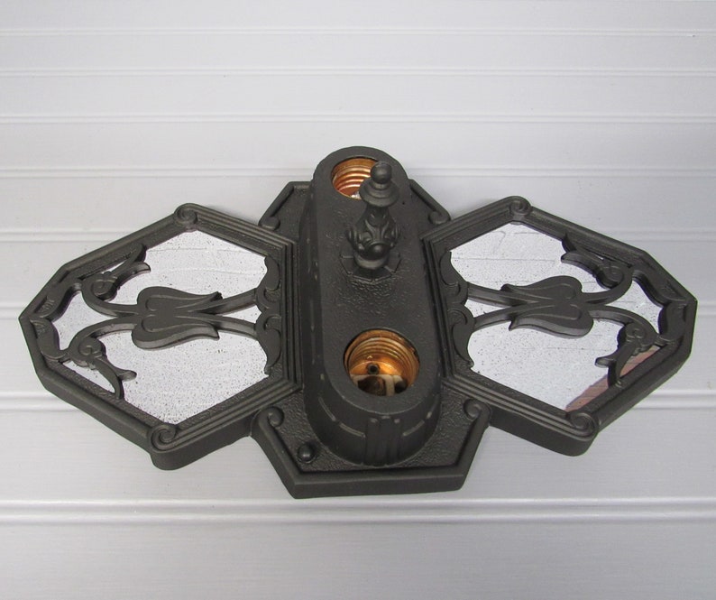 May include: A black metal ceiling light fixture with three decorative glass panels and two light sockets. The fixture has a decorative finial on top.