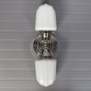 May include: A silver wall sconce with two white frosted glass shades. The sconce has a round base and a decorative design.