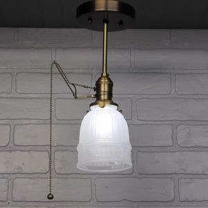 May include: A white frosted glass pendant light fixture with a brass chain pull switch and a brass ceiling mount.