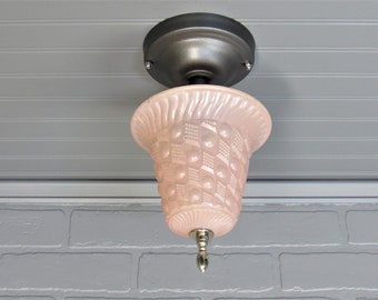 May include: A pink glass ceiling light fixture with a textured, patterned design. The fixture has a black metal base and a silver finial.