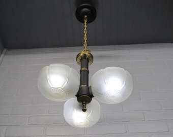 May include: A vintage three-light chandelier with frosted glass shades. The fixture features a dark bronze finish with gold accents and a decorative chain for hanging. The shades are a soft white color.