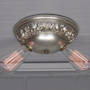 May include: A silver ceiling light fixture with an ornate floral design and two exposed filament light bulbs.