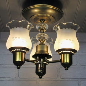 May include: A three-light brass ceiling fixture with frosted glass shades. The shades have a scalloped edge and a floral design.