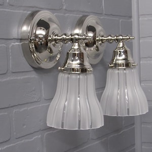 May include: A pair of silver wall sconces with frosted glass shades. The shades have vertical lines and a bell shape.