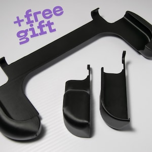 Könnte beinhalten: Schwarzes Kunststoff-Zubehörset, bestehend aus einem langen, gebogenen Teil und zwei kleineren Komponenten. Der Text "+free gift" ist in Lila. Die Teile scheinen für ein Spielgerät oder ein ähnliches elektronisches Produkt zu sein.