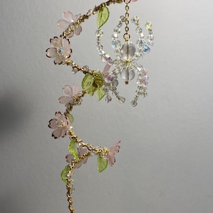 May include: A delicate gold wire sculpture with pink and green glass flowers and a crystal spider hanging from a chain.