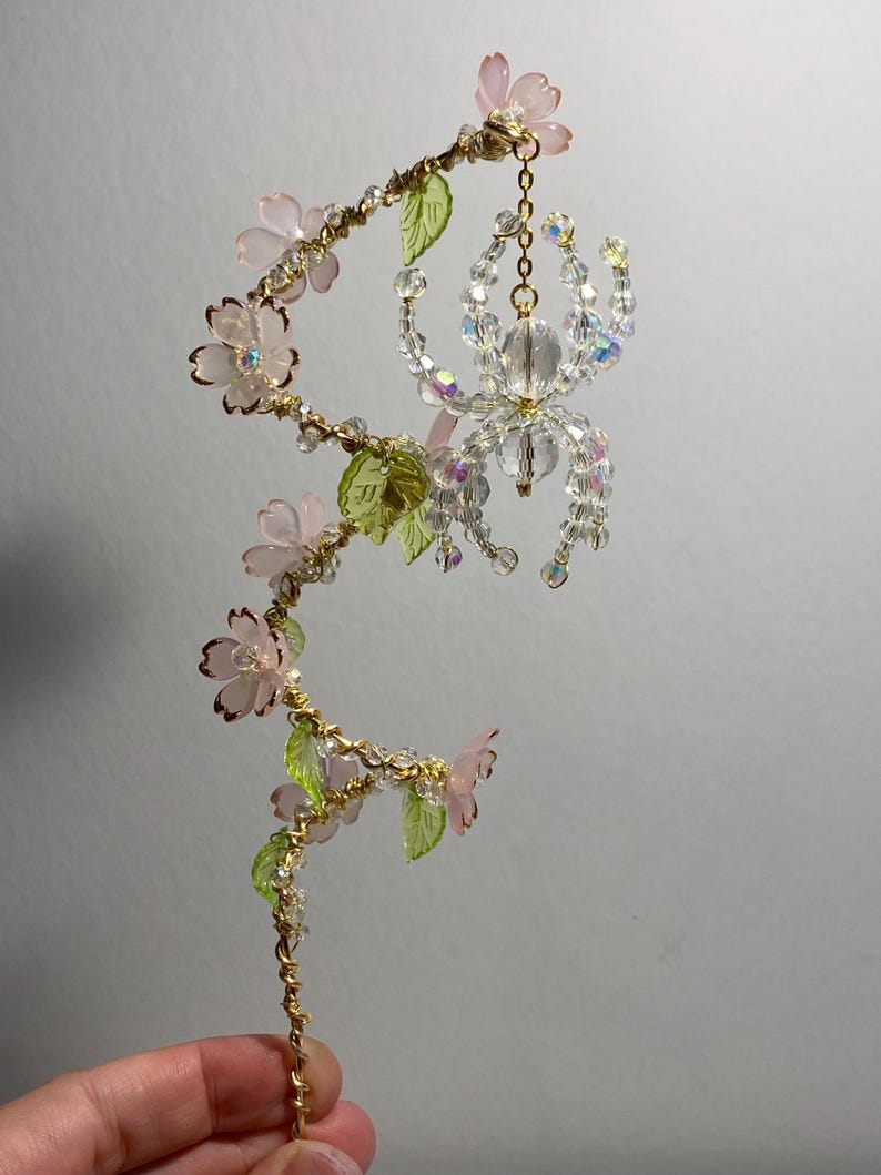May include: A delicate gold wire sculpture with pink and green glass flowers and a crystal spider hanging from a chain.