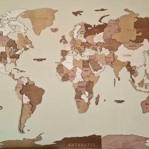 May include: A wooden world map with countries in various shades of brown and beige. The map includes a compass rose and country names. The continents are cut out and mounted on a light-colored background.