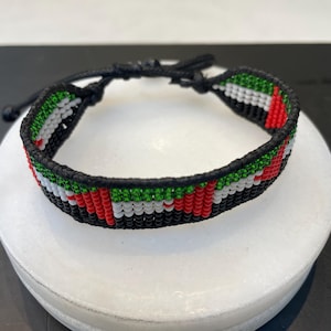 May include: A black beaded bracelet with the colors of the United Arab Emirates flag. The bracelet is made with small, colorful beads and has a black cord closure.