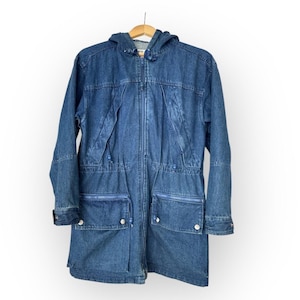 May include: A white ceramic mug with a black handle and the text "But First, Coffee" in a bold, black font. The mug is set against a blurred background, suggesting a cozy setting.