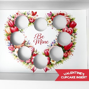 Puede incluir: Inserto para cupcakes blanco con un diseño floral en forma de corazón, corazones rojos y las palabras "Be Mine". El inserto tiene siete recortes circulares para cupcakes y una pancarta roja que dice "Valentine's Cupcake Insert".