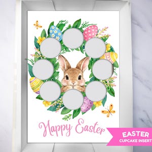 Op de afbeelding: Paas cupcake-inzet met een aquarelontwerp. Een bruin konijn is omringd door een krans van groene bladeren, gele bloemen en kleurrijke paaseieren. De woorden "Happy Easter" zijn in roze geschreven.