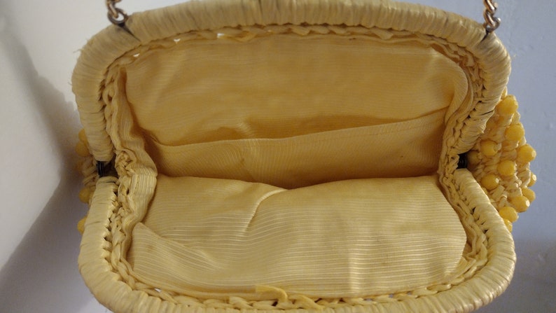 May include: A yellow beaded purse with a woven design and a fabric lining. The purse has a metal clasp and a chain strap.