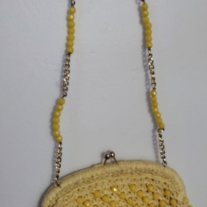 May include: A yellow beaded clutch purse with a gold chain strap. The purse is made of woven straw and has a rounded shape.