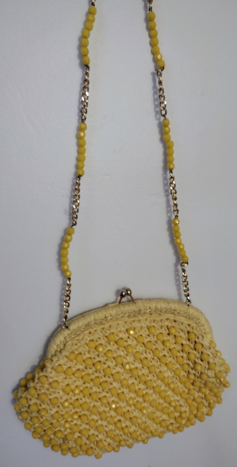 May include: A yellow beaded clutch purse with a gold chain strap. The purse is made of woven straw and has a rounded shape.