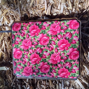 May include: A vintage compact with a floral design featuring pink roses on a green background. The compact has a gold trim and a hinged lid.