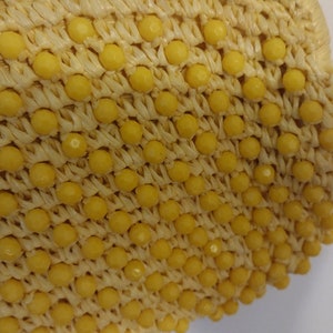 May include: A close-up of a yellow straw bag with a woven texture and yellow beads.