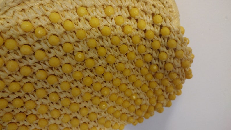 May include: A close-up of a yellow straw bag with a woven texture and yellow beads.
