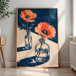 Puede incluir: Una lámina artística enmarcada que muestra dos botellas de vidrio transparente, cada una con una amapola de color naranja vibrante. La composición utiliza un estilo de alto contraste con un fondo azul oscuro texturizado y una superficie beige.