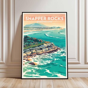 May include: A framed art print featuring a stylized coastal landscape. The artwork depicts Snapper Rocks, Queensland, with turquoise water, a rocky shoreline, and a distant mountain range under a warm-toned sky. The print is in a black frame.