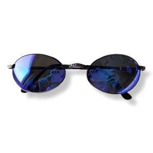 Pode incluir: Óculos de sol de formato oval com lentes refletoras azul-escuras e uma armação metálica fina e texturizada. A ponte e as dobradiças apresentam um padrão gravado distinto, proporcionando um acabamento detalhado à estrutura dos óculos.