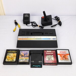 May include: A vintage Atari 2600 video game console with a joystick, power adapter, and several game cartridges. The console is black with a silver stripe and the text "ATARI 2600". Game cartridges include "Video Olympics" and "Baseball".