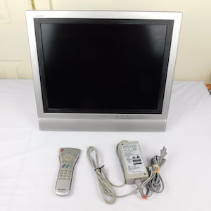 May include: A silver Sharp Aquos flat-screen television with a black screen. The TV has a silver frame and a speaker bar at the bottom. A remote control, power adapter, and power cord are included.