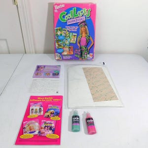 Op de afbeelding: Een Barbie Cool Looks Fashion Designer knutselset met een roze en groene doos, een wit stoffen vel, twee flesjes Tulip-verf en een boekje met instructies en informatie over andere Barbie-softwaretitels.