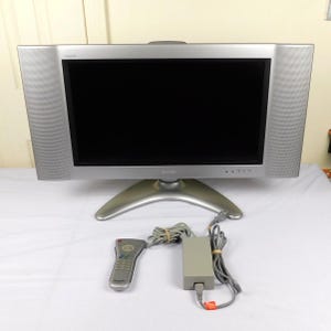 May include: Silver Sharp Aquos television with a black screen, a curved base, and integrated speakers. Includes a remote control and power adapter. The TV is approximately 25 inches wide.