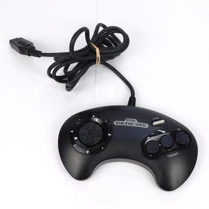 Puede incluir: Un mando de videojuegos Sega Genesis negro que cuenta con un pad direccional circular, tres botones de acción etiquetados como A, B y C, un botón Start blanco y un cable negro largo con un conector en el extremo del cordón.