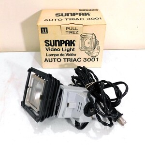 Peut inclure: Un projecteur vidéo Sunpak Auto Triac 3001 vintage avec sa boîte d'origine. La lampe est argentée et noire, avec une source lumineuse carrée et un cordon noir. La boîte est beige avec du texte noir et un schéma de la lampe.