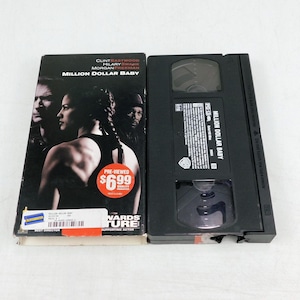 May include: A VHS tape of the movie "Million Dollar Baby" with Clint Eastwood, Hilary Swank, and Morgan Freeman. The cover features a photo of the actors. The tape is black with a white label. The price tag reads $6.99.
