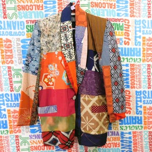 May include: A patchwork blazer with a variety of patterned fabrics in orange, blue, red, and purple. The blazer has a notched lapel, two pockets, and a single button closure. The background features a repeating pattern of team names.