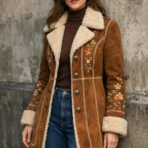 May include: A brown suede coat with cream-coloured faux fur trim on the collar, cuffs, and interior. The coat has floral embroidery in orange and yellow, and gold buttons. A stylish outerwear piece.