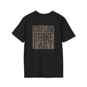 May include: Black t-shirt with the text "STAY LOW STRIKE FAST" in a distressed, tan-colored square. The text is centered on the shirt and has a military-inspired aesthetic. The shirt is made of a soft material.