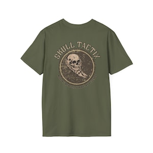 May include: Olive green t-shirt with a circular graphic featuring a skull and the words "SKULL TACTIX". The graphic also includes the phrases "RISE AS REBELS" and "STRIKE AS LEGENDS".