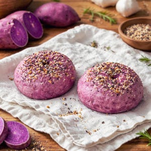 May include: Two purple bagels topped with seeds and spices sit on a white cloth. Sliced purple sweet potatoes are next to the bagels. Other ingredients like garlic and herbs are in the background. The bagels are a vibrant purple color.