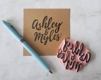 May include: A close-up of a brown card with the text "Ashley & Myles" written in black cursive. A pink rubber stamp with the same text is also shown.