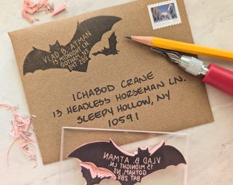 Pode incluir: Um envelope de papel kraft castanho com um carimbo de remetente preto em forma de morcego com o texto Vlad B. Atman, 13 Midnight Ln., Gotham, NS, B4T 2B8. Inclui um lápis amarelo, uma ferramenta de escultura e um bloco acrílico transparente.