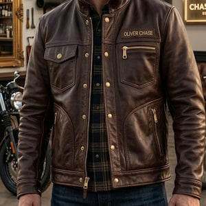 Pode incluir: Uma jaqueta de couro marrom escuro com gola alta, zíper central e botões de pressão dourados. A jaqueta inclui dois bolsos no peito, dois bolsos inferiores com zíper e um emblema retangular com o texto OLIVER CHASE.
