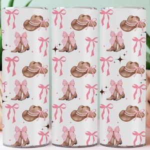 Puede incluir: Tres vasos blancos con un patrón repetido de sombreros de vaquero marrones con adornos de perlas, lazos rosas y botas de vaquero marrones con lazos rosas. Los lazos rosas y las explosiones de estrellas completan el diseño.