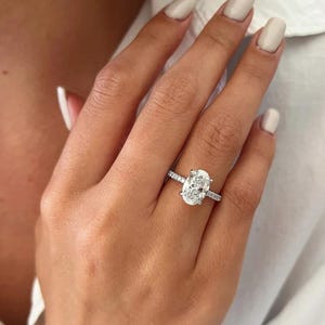 Könnte beinhalten: Ein silberner Ring mit einem großen ovalen Diamanten, der in einer Pavé-Fassung sitzt. Der Ring befindet sich an einem Finger.