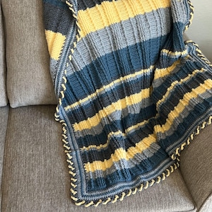 May include: A striped crocheted throw blanket in shades of blue, gray, and yellow with a crocheted border. The blanket is draped over a gray couch.
