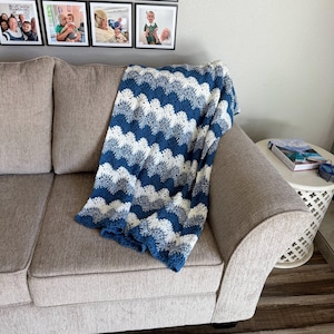 May include: A blue and white crocheted blanket with a wavy pattern is draped over a light gray couch.