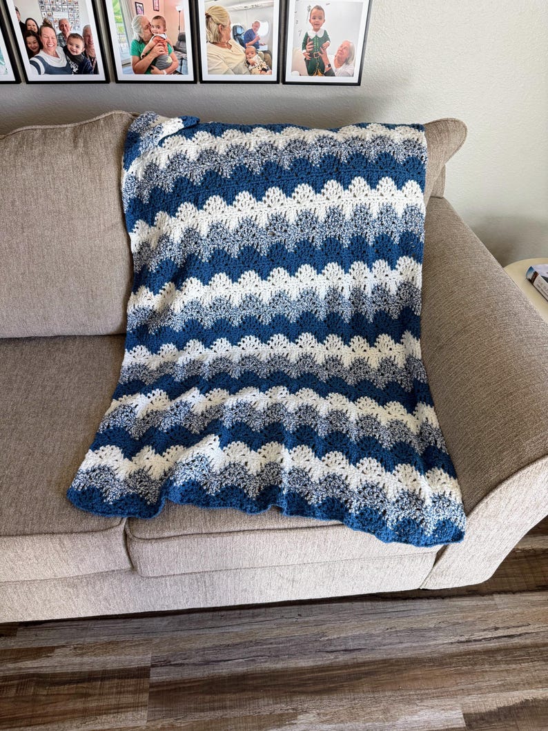 May include: A blue and white crocheted blanket with a wave pattern. The blanket is folded and placed on a light brown couch.