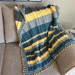 May include: A striped crocheted throw blanket in shades of teal, gray, and yellow with a yellow crocheted border.